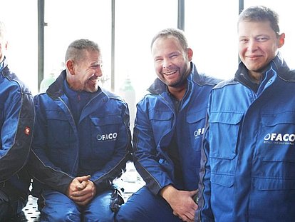 Mitarbeiter in Arbeitskleidung von FACO Metalltechnik sitzen an einem Tisch und lachen